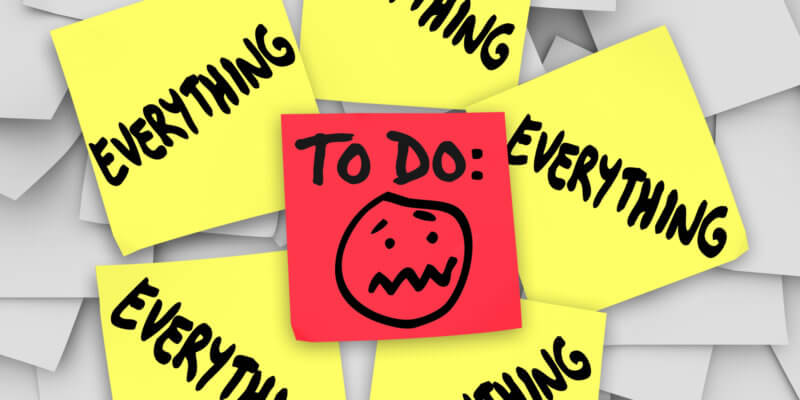 The background is a collection of miscellaneously placed white squares that look like sticky notes. On top of that pile are five yellow sticky notes with the word “Everything” hand printed on each note. In the center, there is one red square with a cartoon face in the middle and the words “To Do” above the face. The face seems overwhelmed.