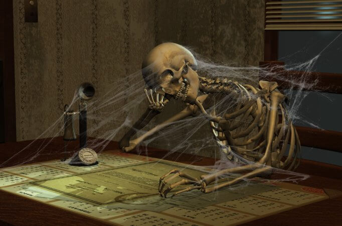 Picture of a skeleton over a desk with a phone from the early 1900. There are cobwebs over the skeleton.