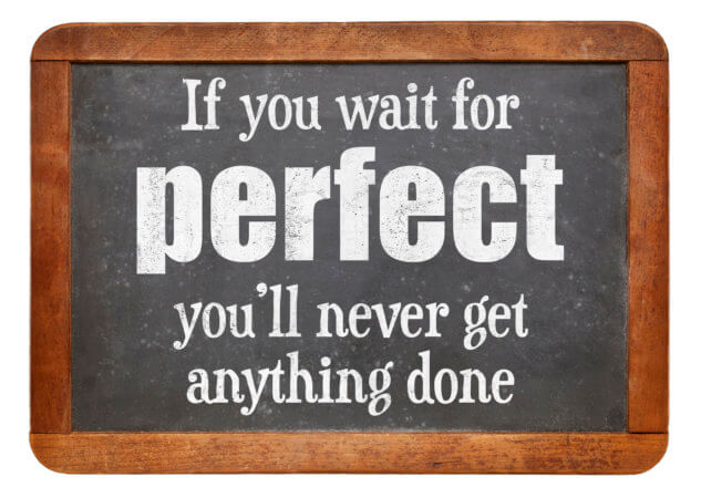 Small blackboard with wood frame. On the blackboard is the comment "If you wait for perfect your never get anything done".Perfectionism delays progress