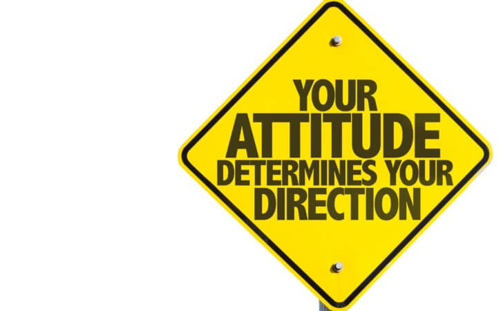 Diamond-shaped yellow street sign with these words in black on the yellow background: Your attitude determines your direction.