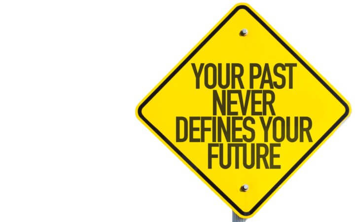 Yellow diamond-shape sign on a white background with the words "Your past never defines your future".
