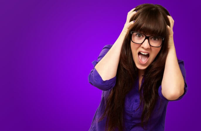 Long-haired woman wearing glasses who is grabbing her head and seems to be screaming